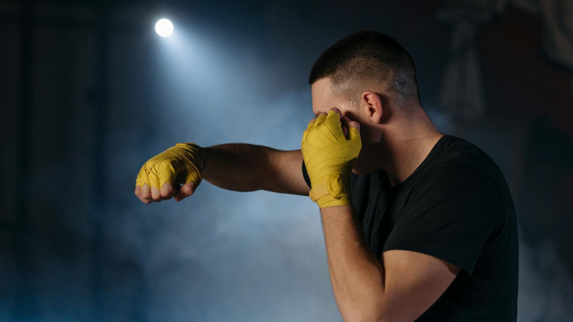 Man in a focused stance performing a strength exercise in a dark, atmospheric setting.